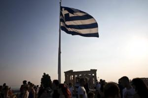 Greek flag flutters in the wind above tourists visiting the archaeological site of the Acropolis hill in Athens, Greece